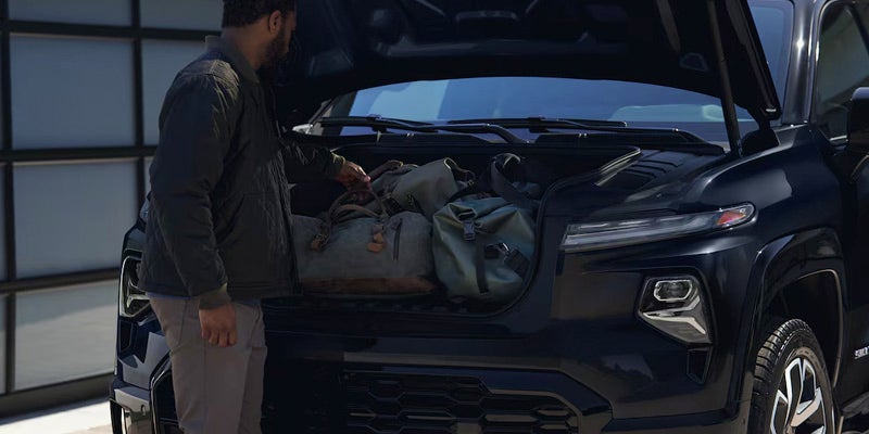 Black 2025 Chevrolet Silverado EV with hood / trunk open and man putting in luggage